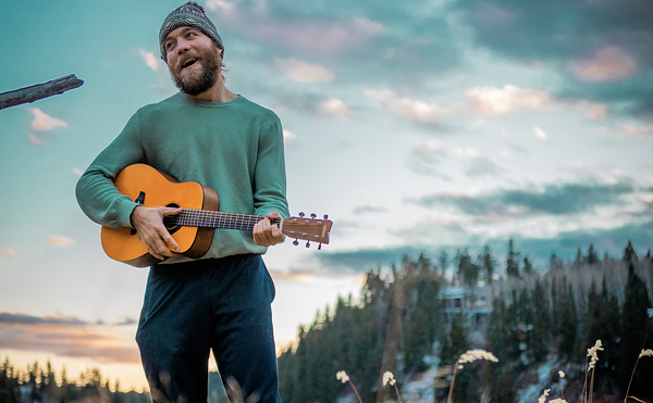man holding a guitar in front of a lake