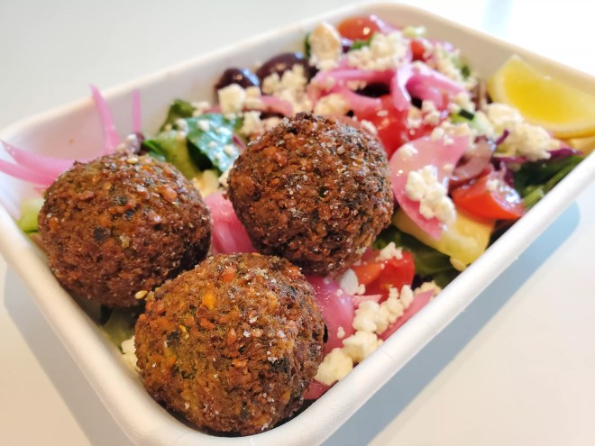 three falafel on top of a salad with onions, feta, lettuce and tomatoes