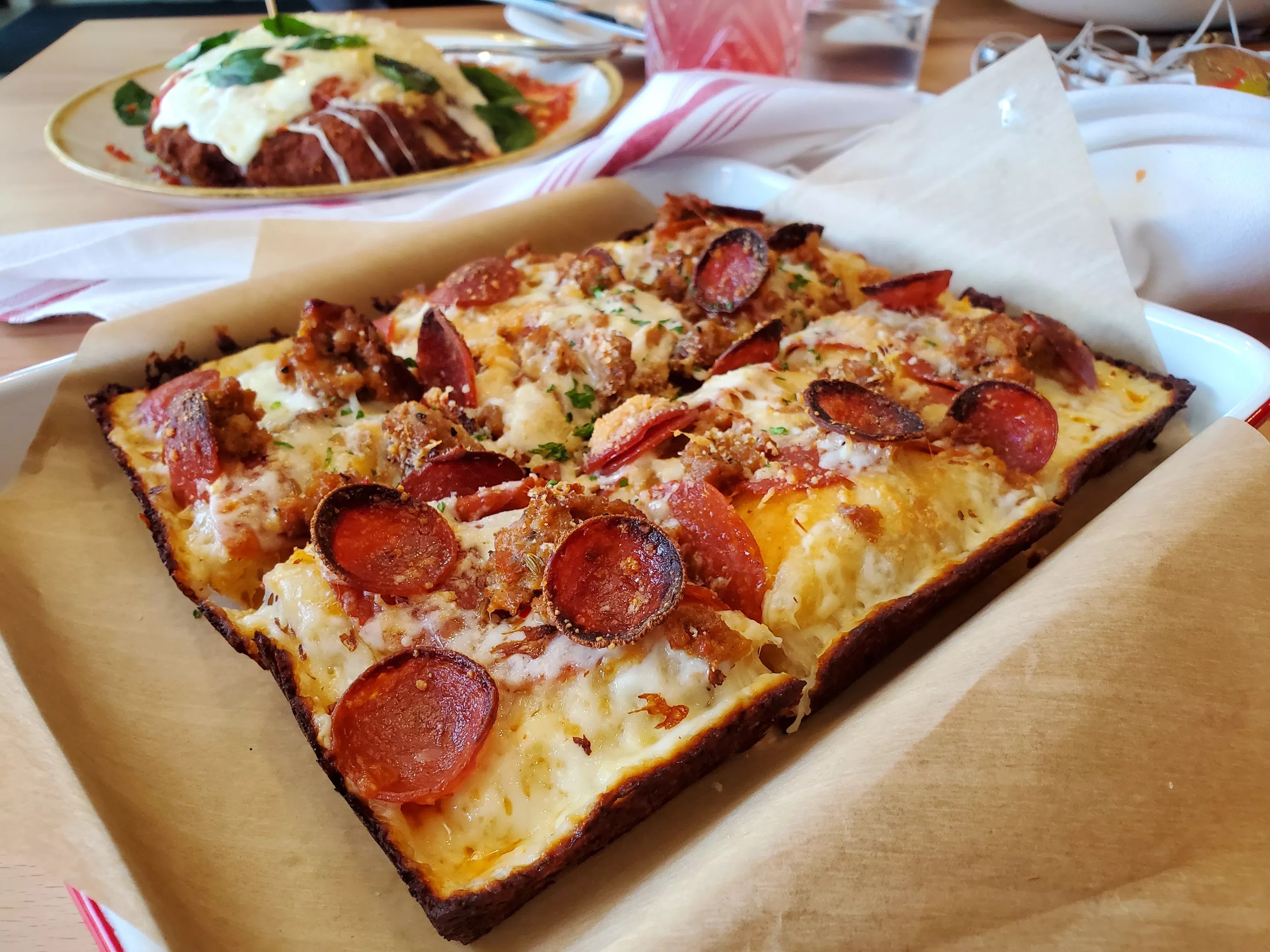 a square cut rectangular pizza with pepperoni and sausage