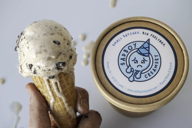 a hand holding an ice cream cone next to a pint of ice cream