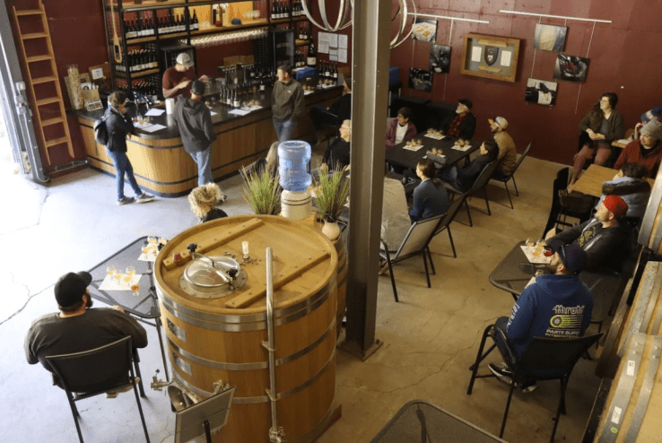 people sitting at tables in a room with a big wooden barrel