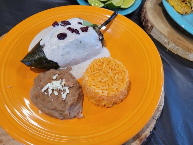 orange plate with chile relleno, rice and beans