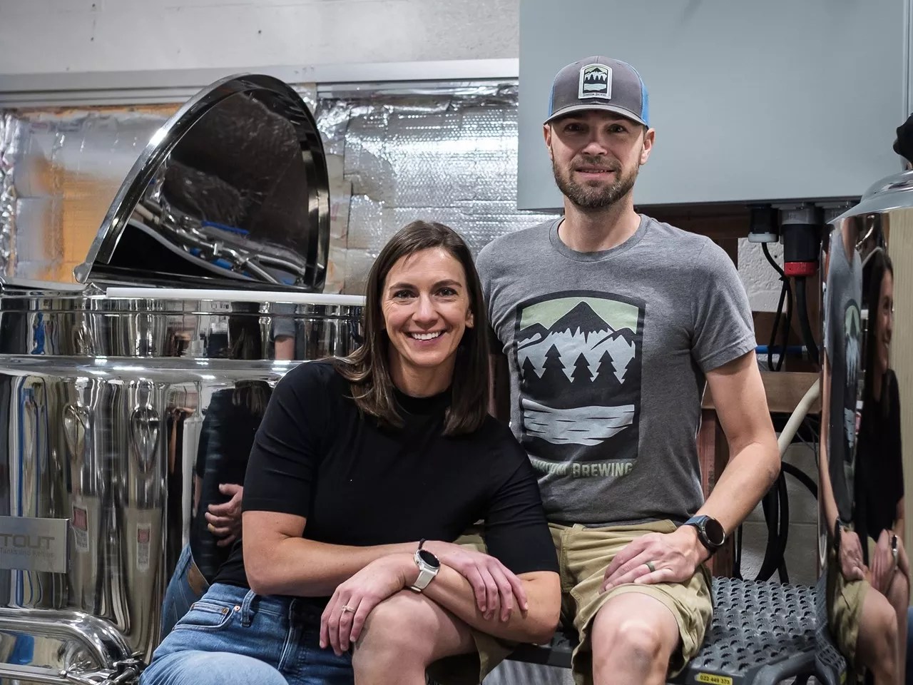 a woman and a man sitting on step ladders in front of brewing equipment