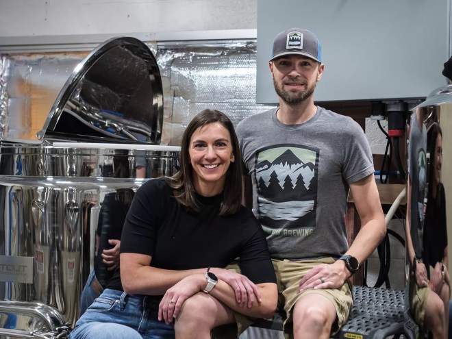 a woman and a man sitting on step ladders in front of brewing equipment