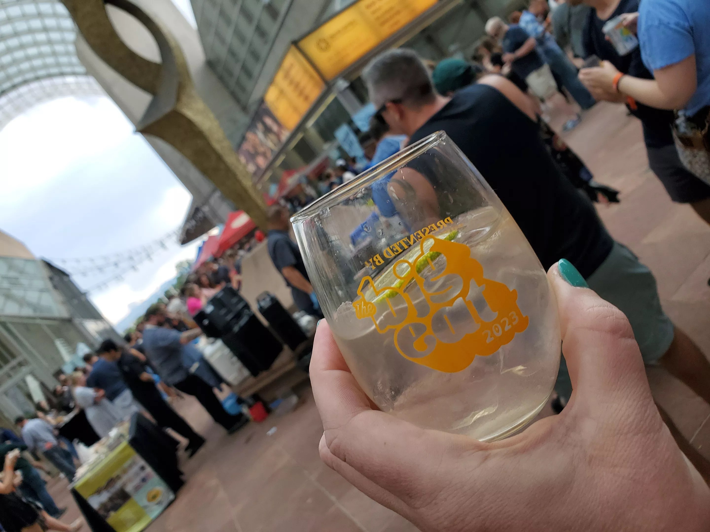hand holding a glass in front of people standing near a statue