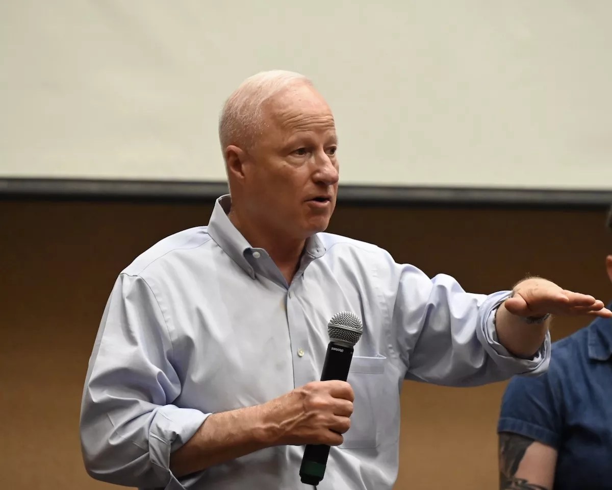 Aurora Mayor Mike Coffman speaks with a microphone in his hand at a town hall.