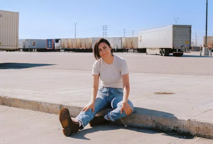 woman in white t-shirt and blue jeans sitting in an empty parking lot.