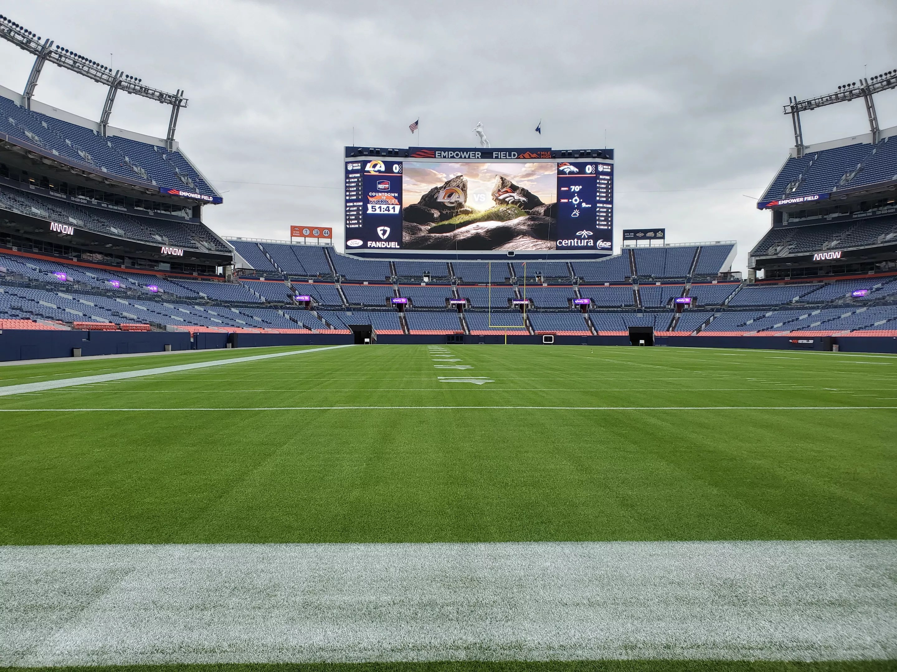 A giant scoreboard at the end of a stadium with a grassy field.