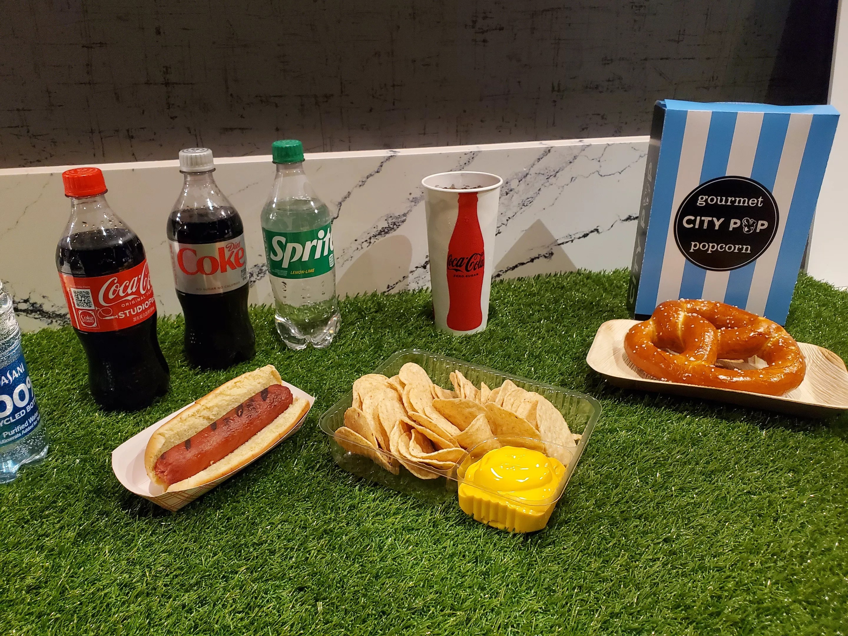 bottles of soda, a hot dog, nachos, a bag of popcorn and a soft pretzel