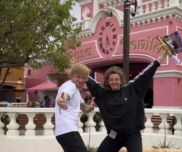 a man and woman strike poses outside of a pink building
