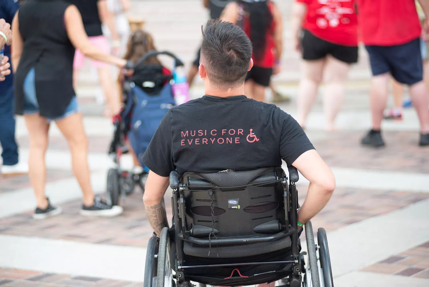 Man in a wheelchair facing away with blurred bodies in front of him.