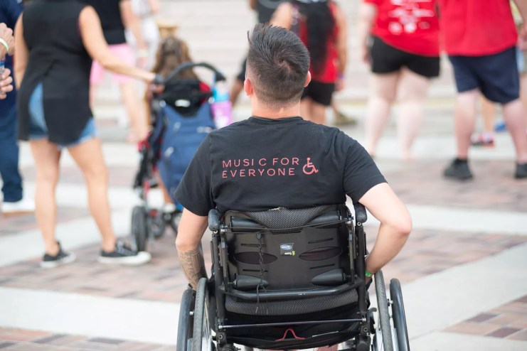 Man in a wheelchair facing away with blurred bodies in front of him.