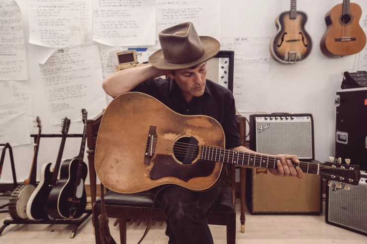 man in fedora poses with his acoustic guitar