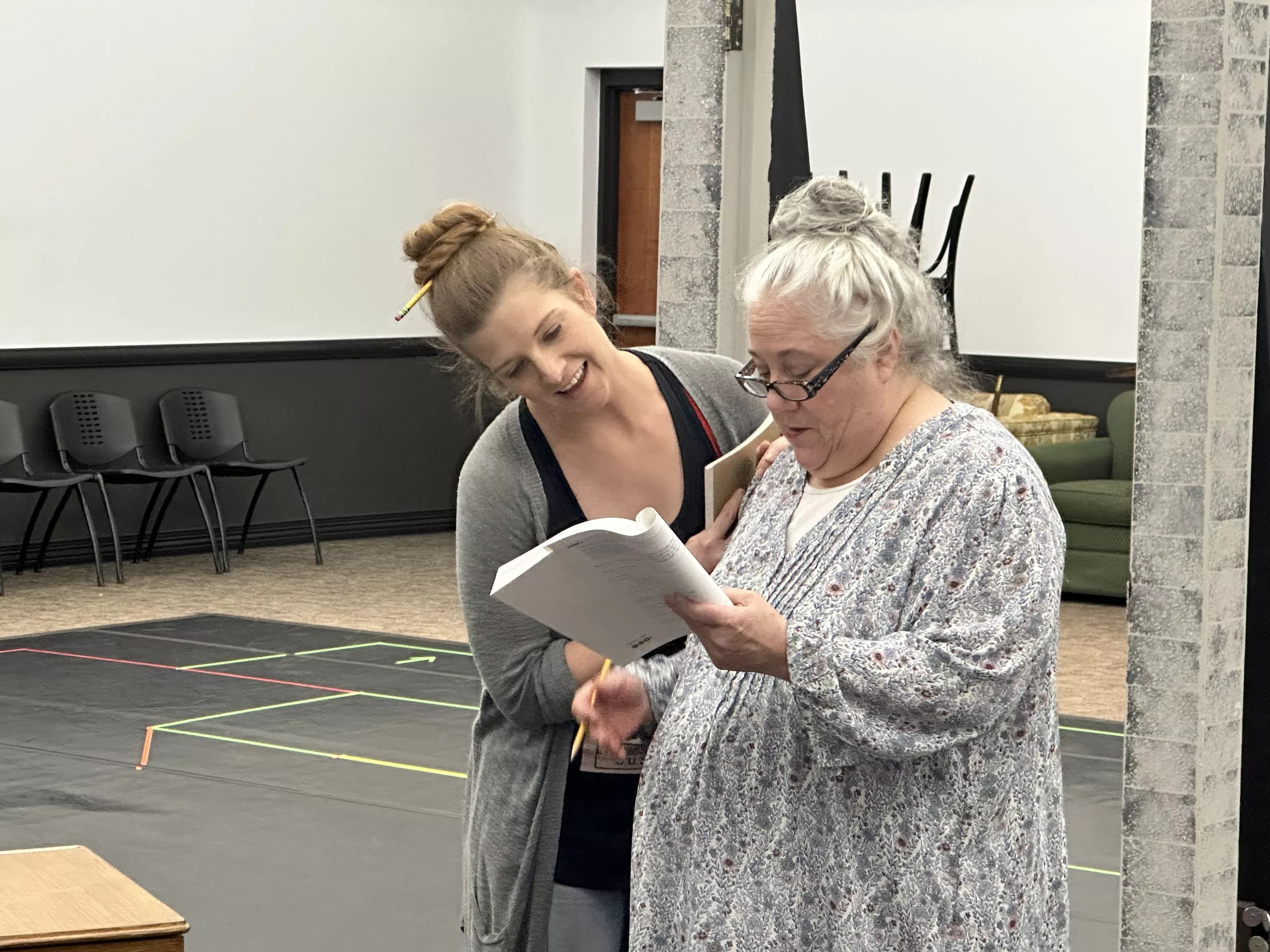 a young woman leans over an elderly woman and the pages she's reading
