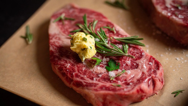 a raw steak with butter and rosemary on top