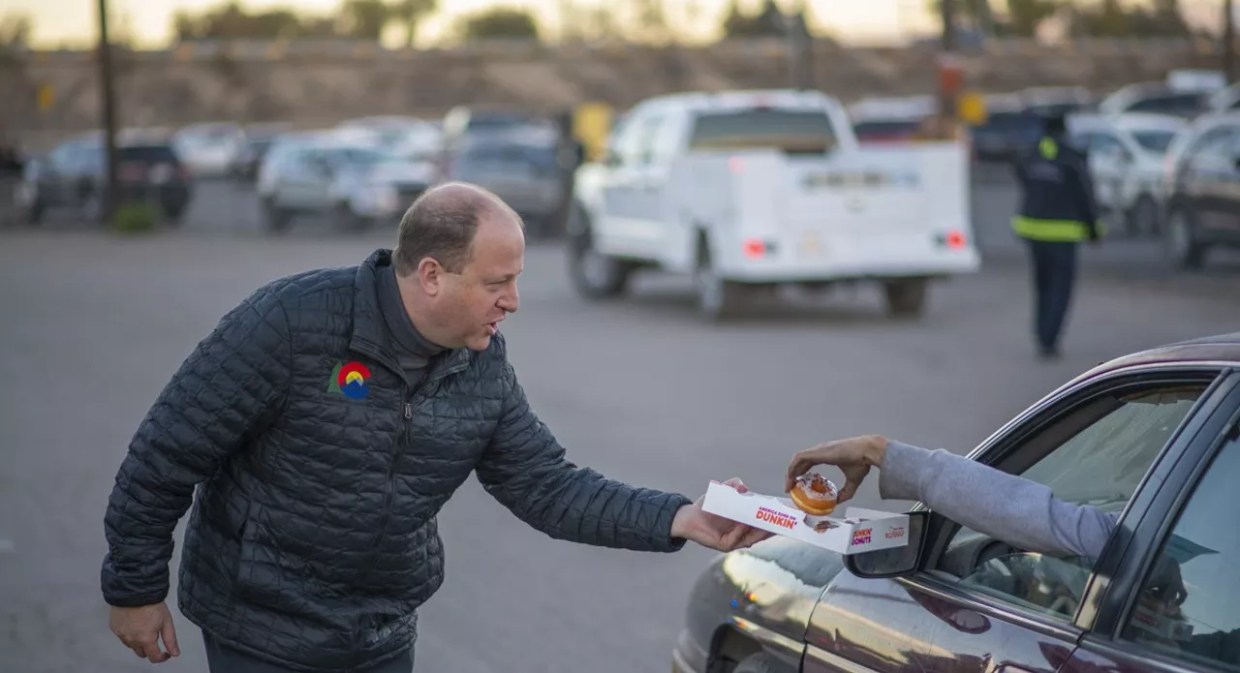 Colorado Governor Jared Polis hands out free doughnuts to a driver