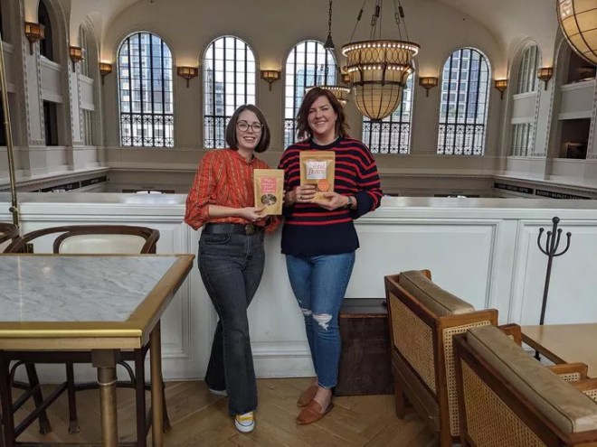 two woman standing, each holding a food package