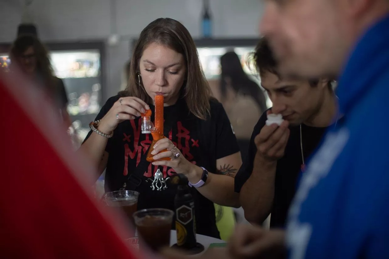 A woman hits weed from a bong as a man smells rosin