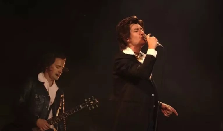 man plays guitar while another sings into a microphone