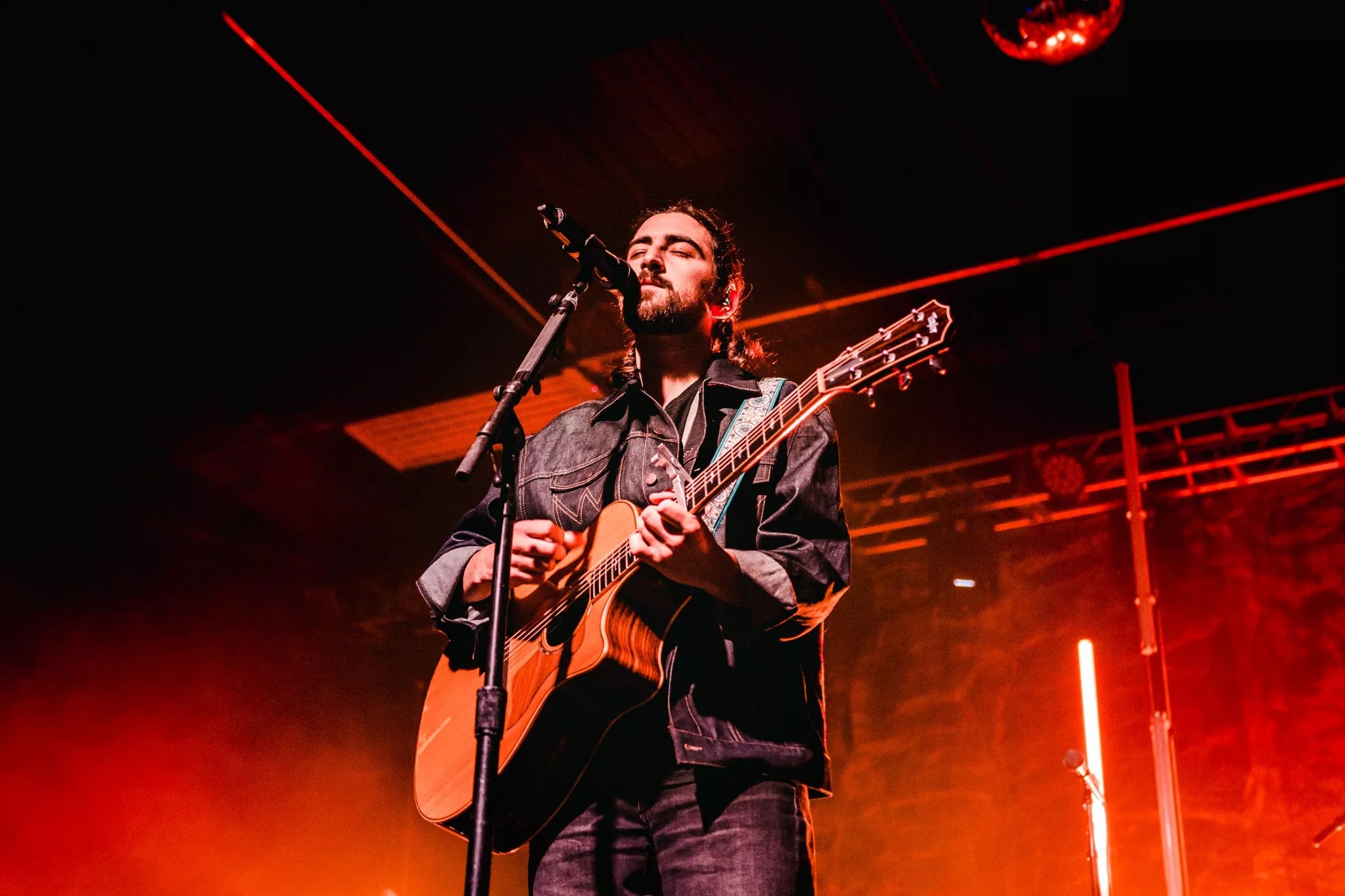 man with guitar singing into a microphone against a red background