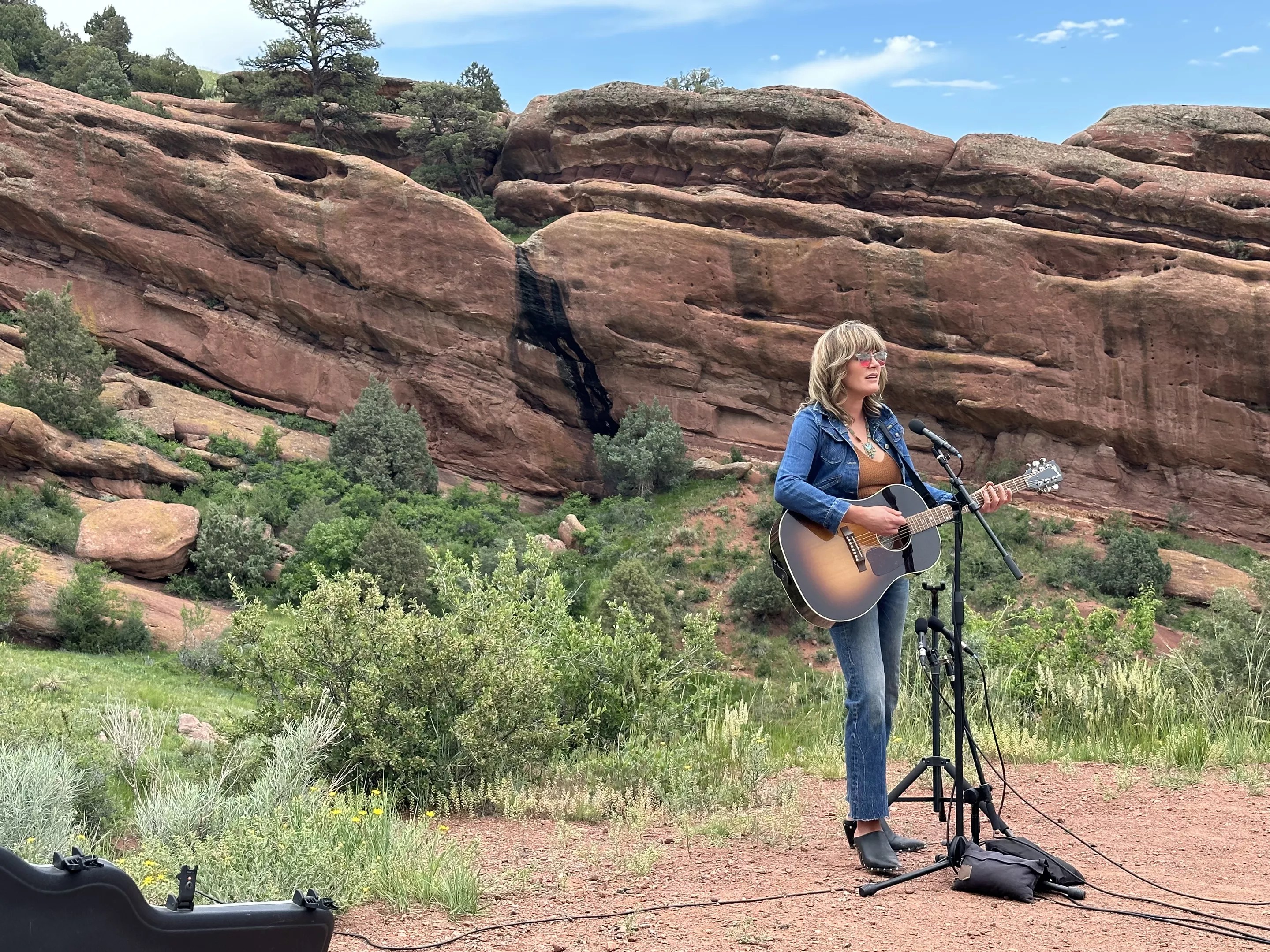 Musician with guitar playing in front of rock face.