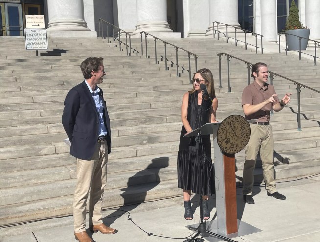 A man in a blue blazer and khakis converses with a woman wearing a long black dress behind a podium.