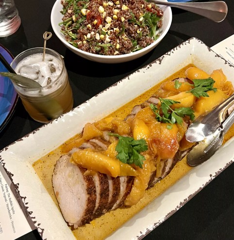a pork roast on a plate next to a cocktail
