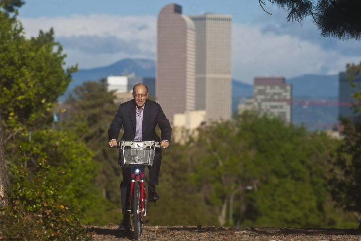 man on bicycle, denver skyline in background.