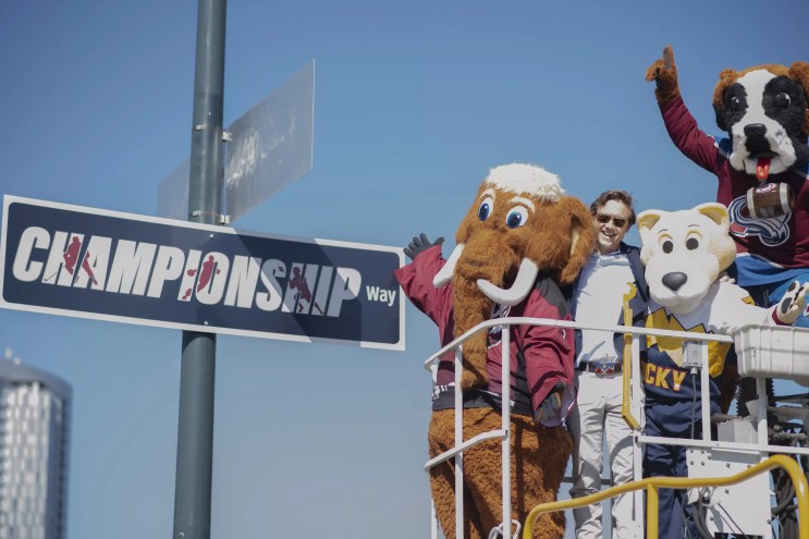 Several mascots and a man stand next to a sign that reads "Championship Way."