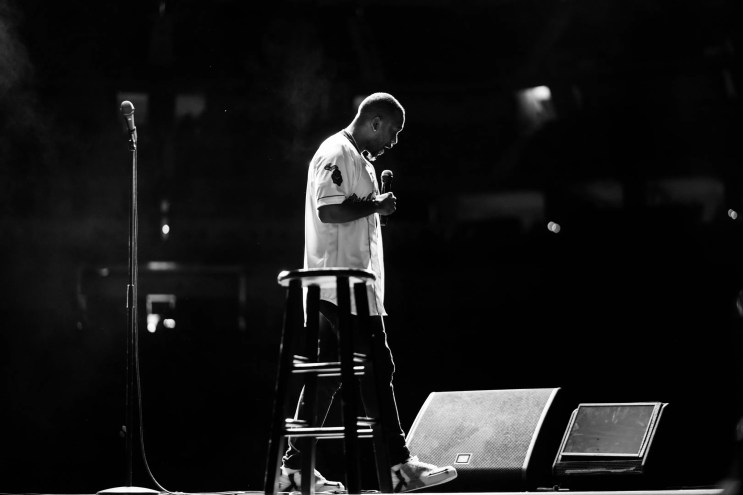 man in white t-shirt standing on stage with microphone