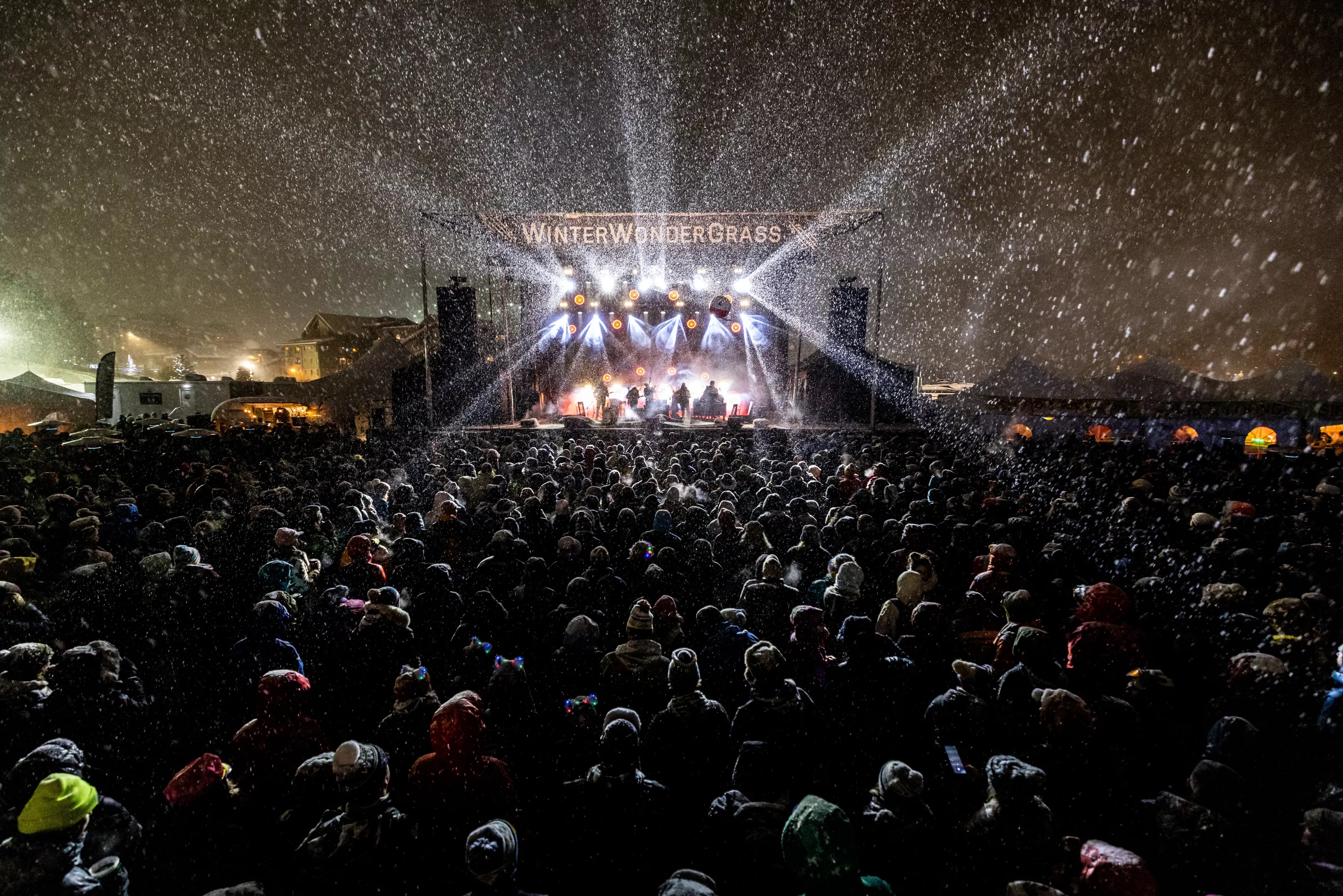 a stage with the words WinterWonderGrass is surrounded by an audience in the snow