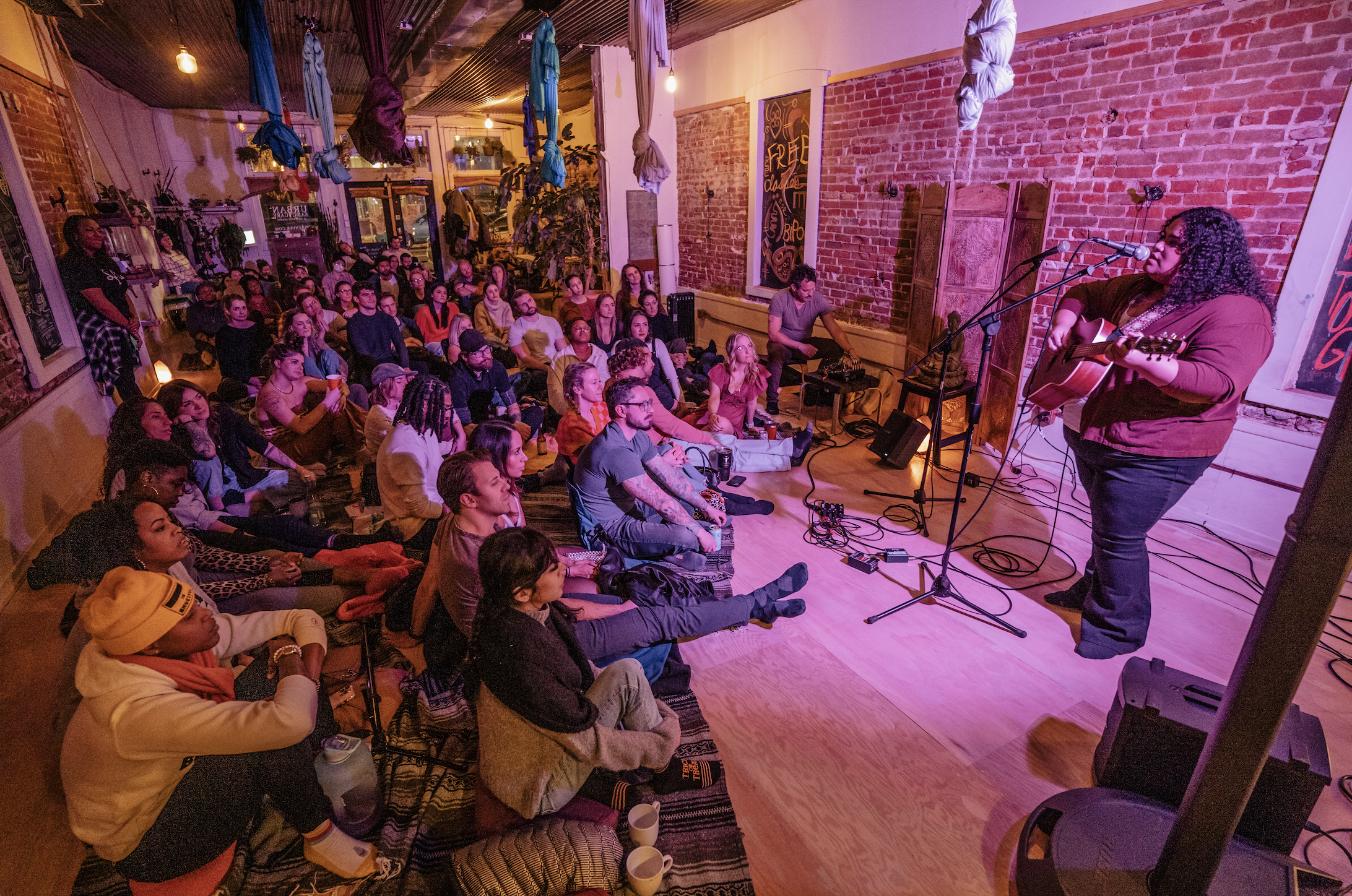 woman playing guitar on intimate stage with pink lighting.