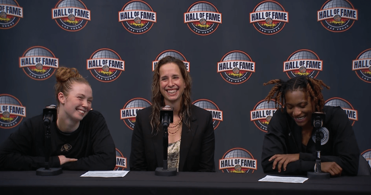 Three women dressed in black sit at a table behind microphones.