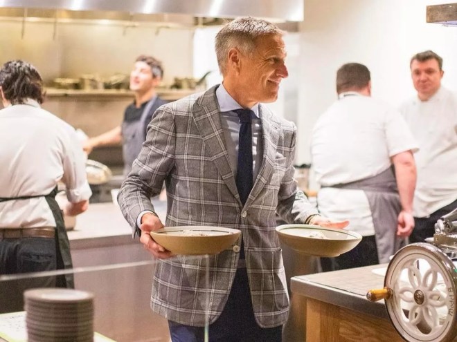 a man in a suit holding plates in a kitchen