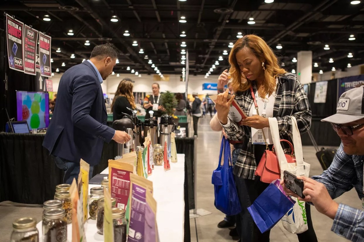 A woman looks at hemp tea as a man takes a photo at the 2023 NoCo Hemp Expo