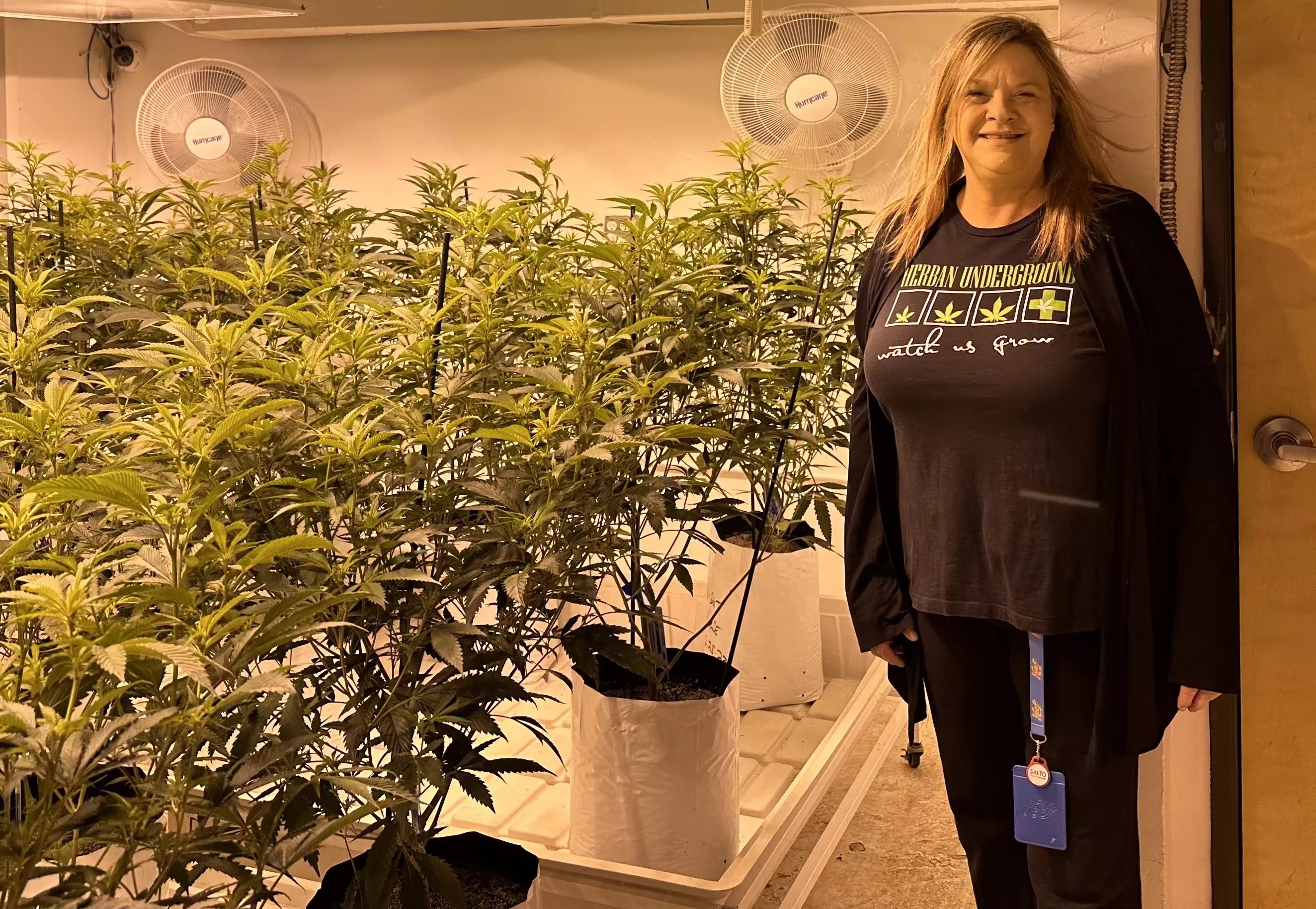 Woman stands in front of indoor marijuana plants