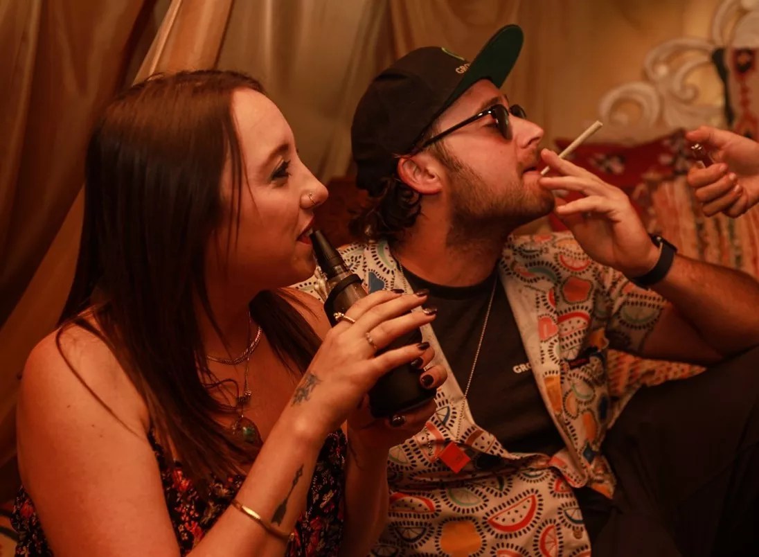 Man smokes a joint as a woman dabs a Puffco Peak
