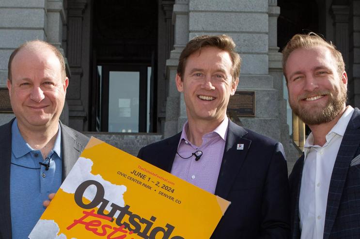 Three men stand and smile.