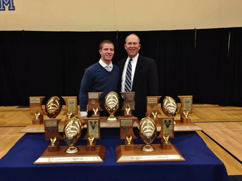 two men in formal attire stand in front of trophies