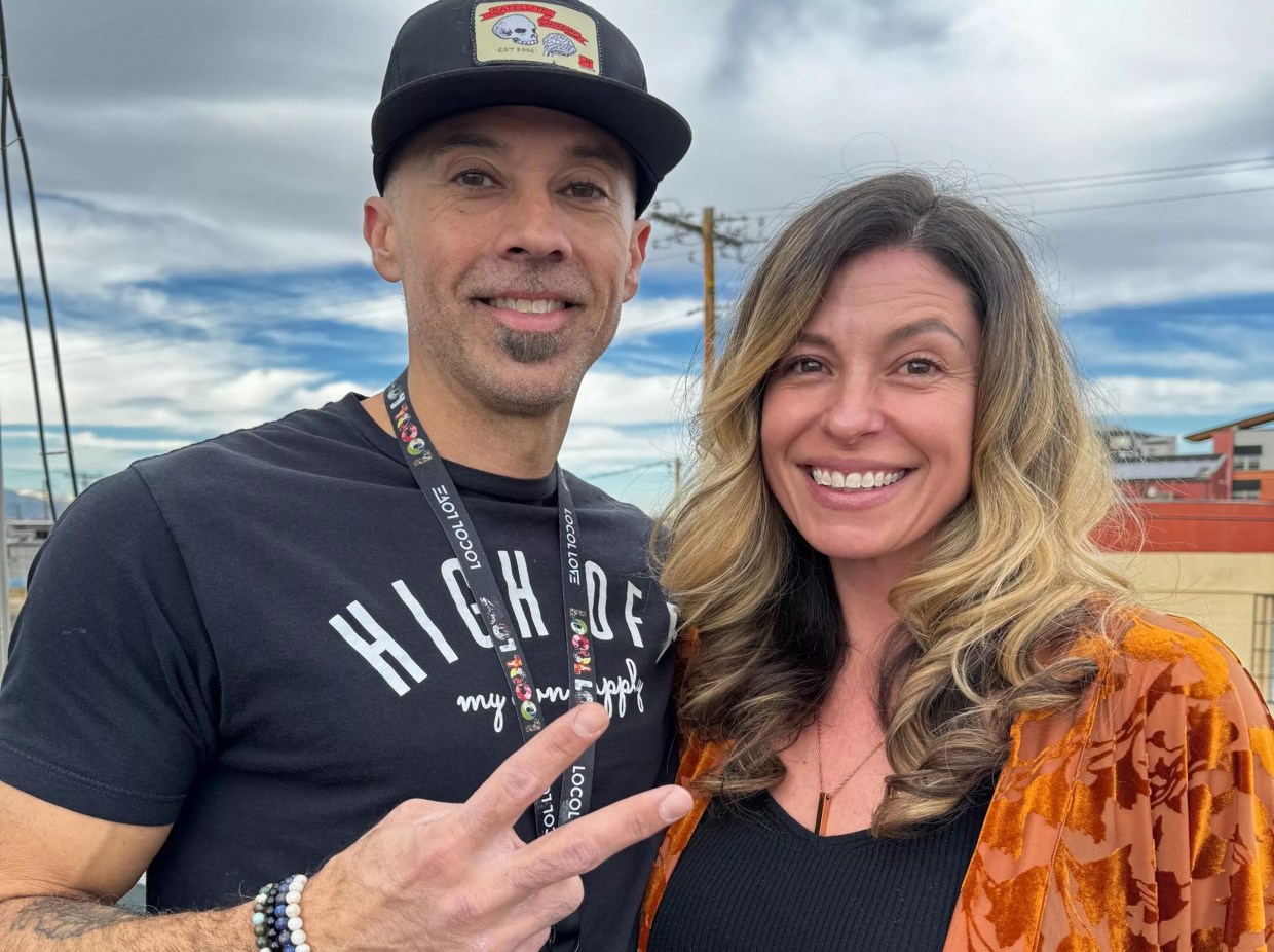 husban and wife pose, man makes a peace sign