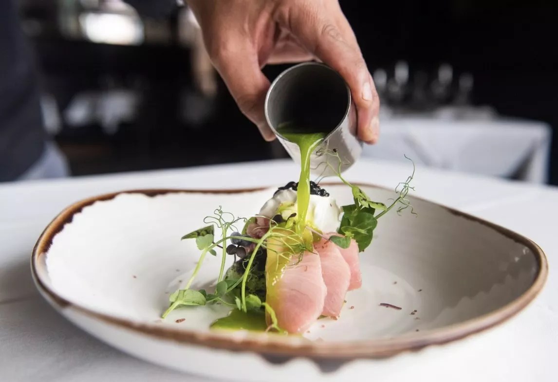 A hand pouring cucumber leche de tigre on hamachi
