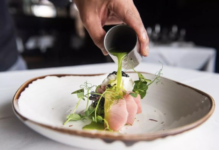 A hand pouring cucumber leche de tigre on hamachi