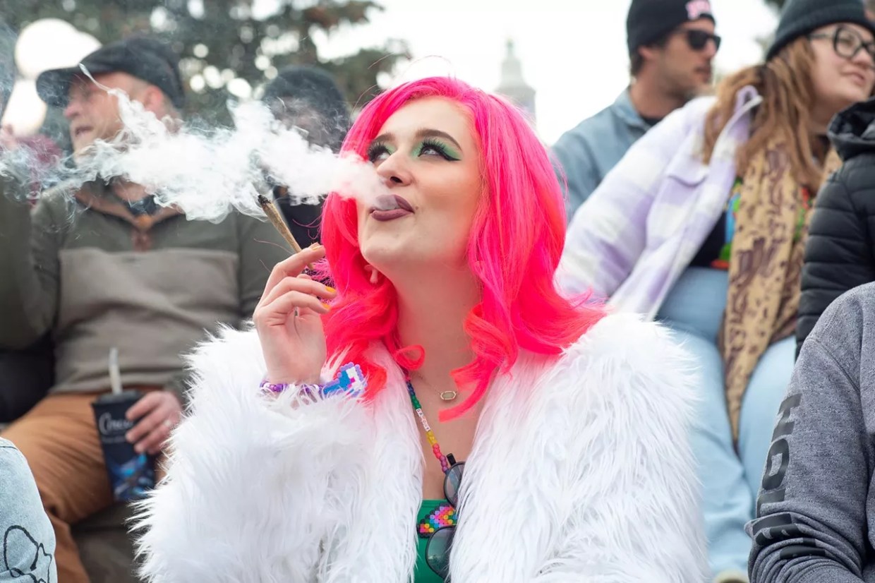Woman with pink hair and white fur coat smokes weed