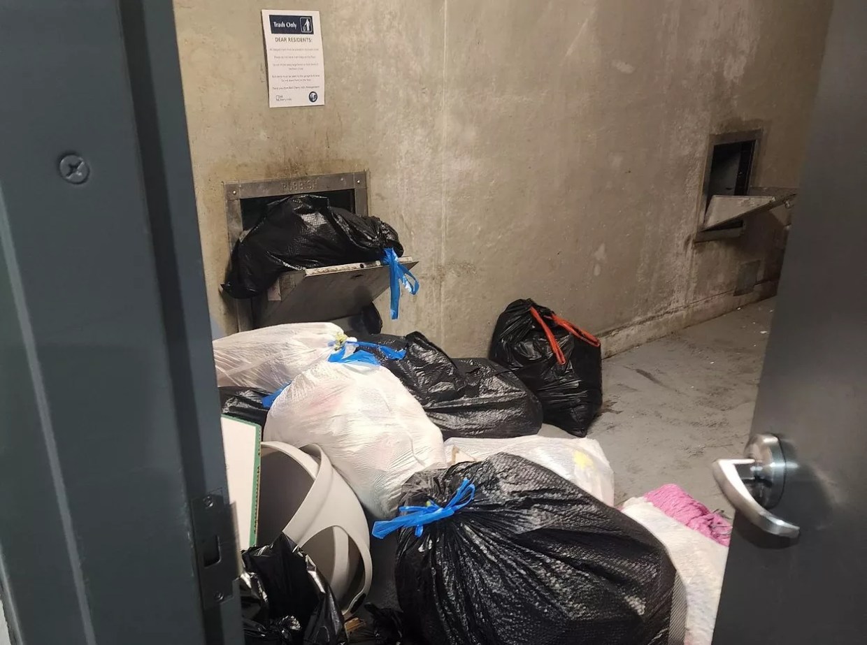 Trash bags overflow out of a garbage chute