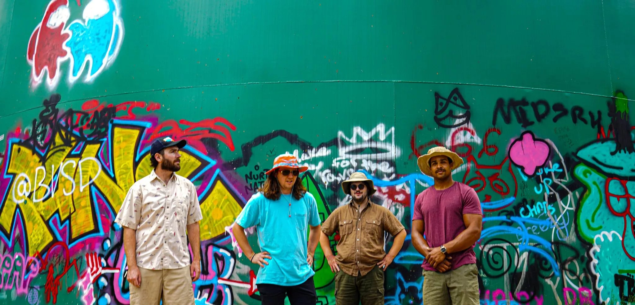 bandmates pose against a green wall with graffiti