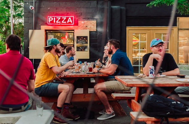 people sitting at picnic tables under a "pizza" sign