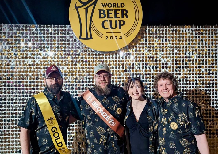 four people posing in front of a world beer cup sign