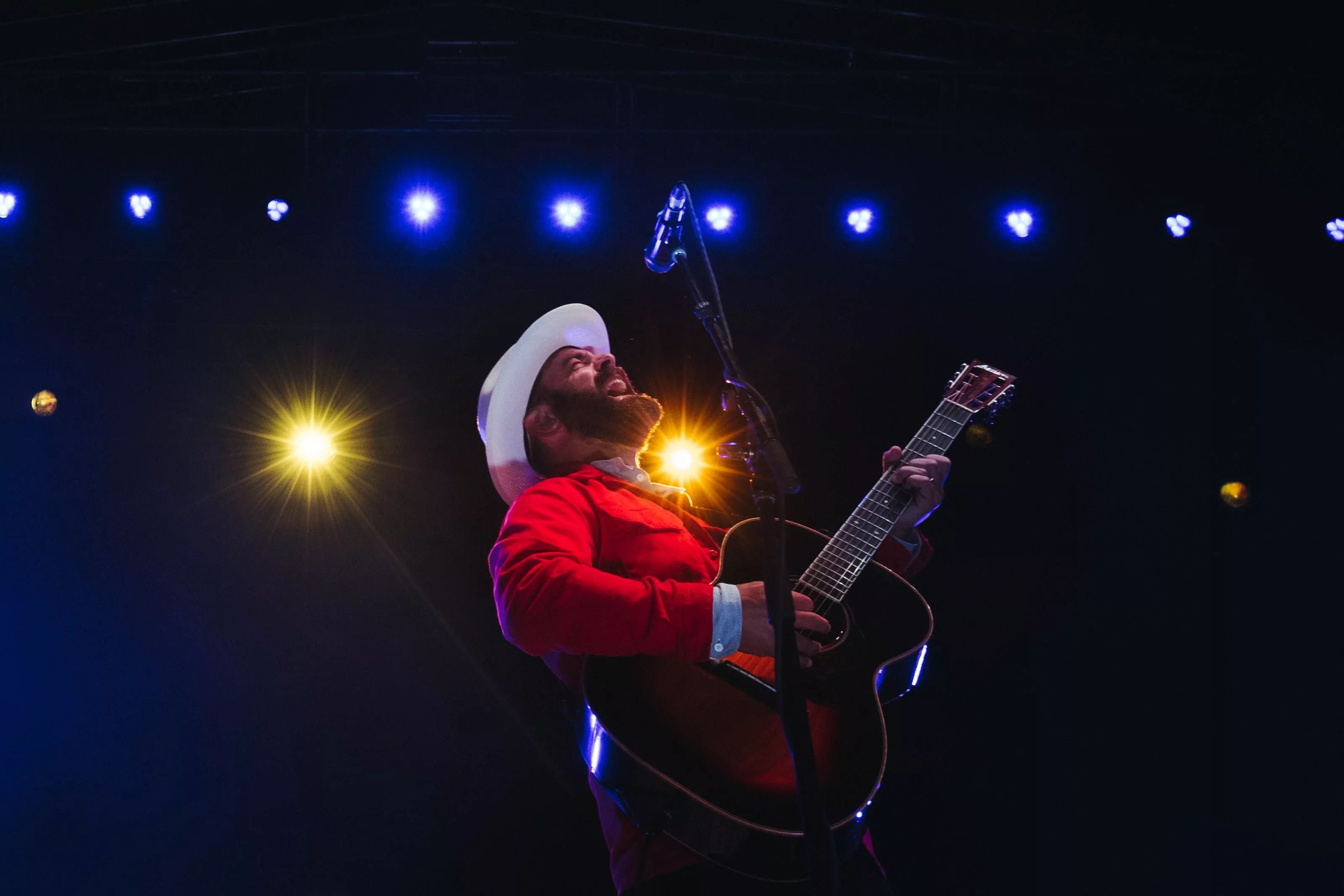 man in white hat and red shirt playing the guitar