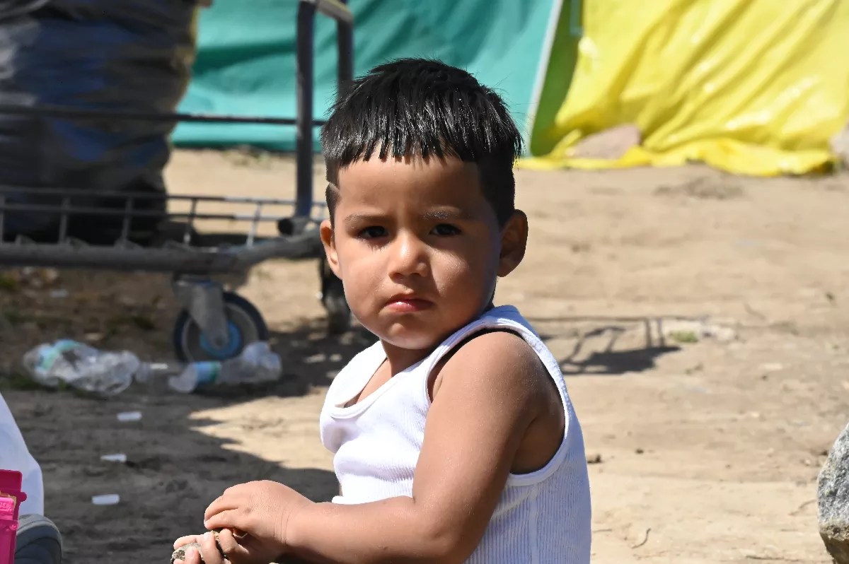 A kid sits in an encampment.