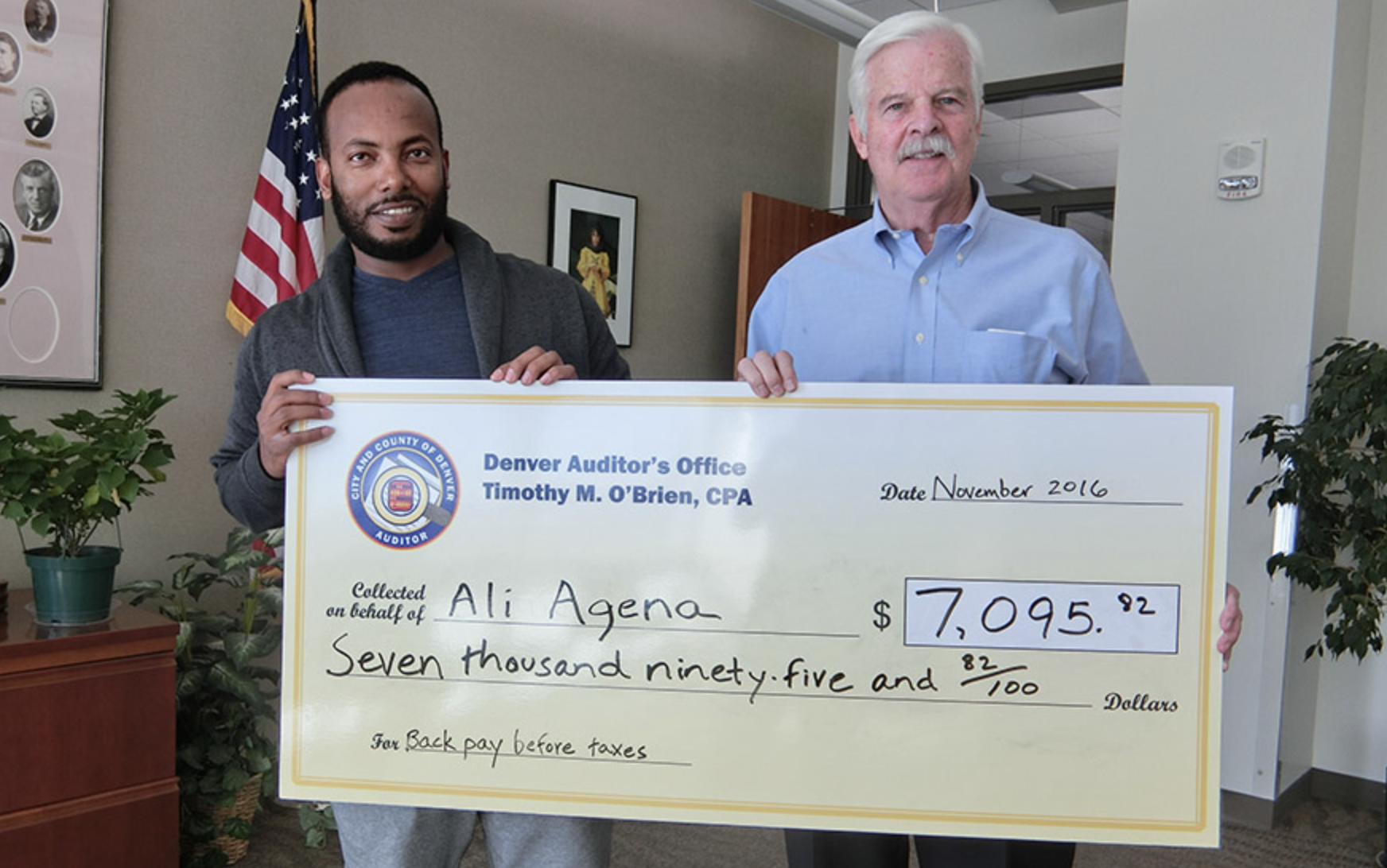 Auditor Tim O'Brien posing with large bank check with a wage theft victim.